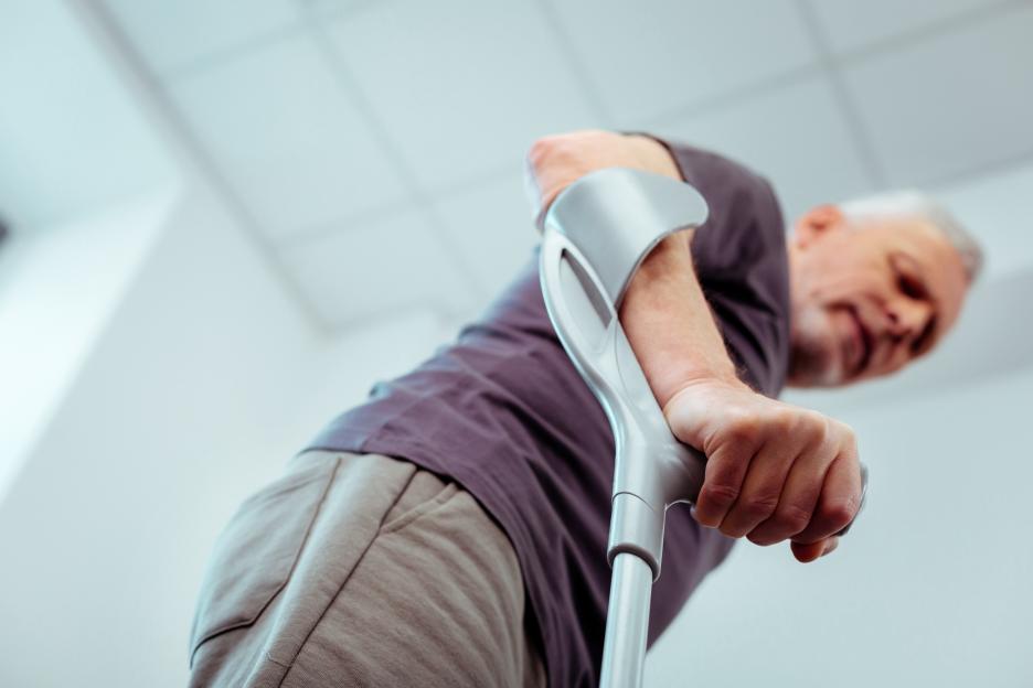 A low-angle, selective focus shot of a man's hand holding crutches.