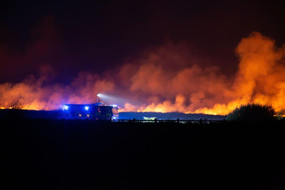 A wildfire burning across a field at night as firefighters work to contain it in Merthyr Tydfil, Wales.