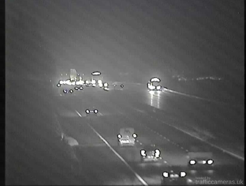Traffic camera displaying vehicles on a wet motorway at night.