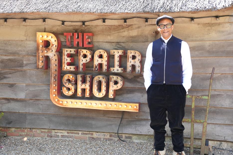 Jay Blades standing in front of "The Repair Shop" sign.