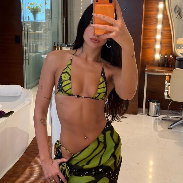 Dua Lipa takes a mirror selfie wearing a green and black butterfly print bikini and sarong.