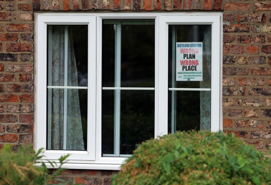 A "Wrong Plan Wrong Place" sign protesting an asylum center in a home's window.