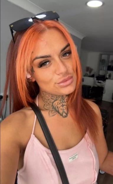 Kelsey Bainbridge, a woman with bright orange hair and tattoos on her neck, is wearing a light pink tank top and sunglasses on her head.