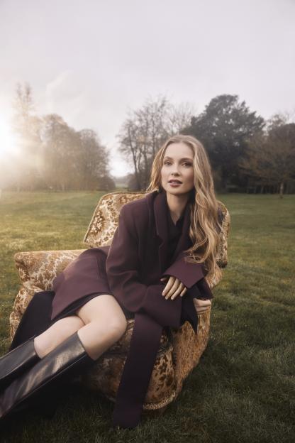 Hannah Dodd of Bridgerton, with long blonde hair, sitting in a patterned armchair in a grassy field.
