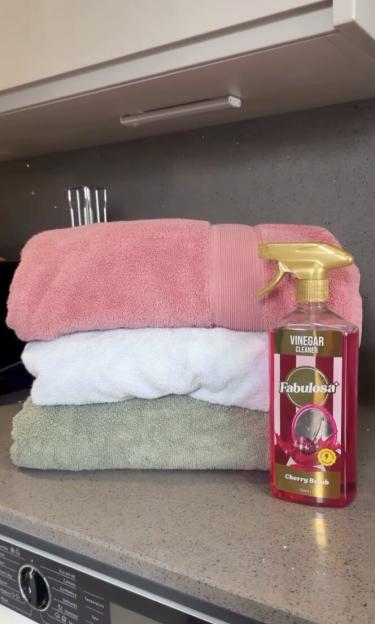 Three folded towels and a bottle of Fabulosa Cherry Bomb Vinegar Cleaner on a countertop.