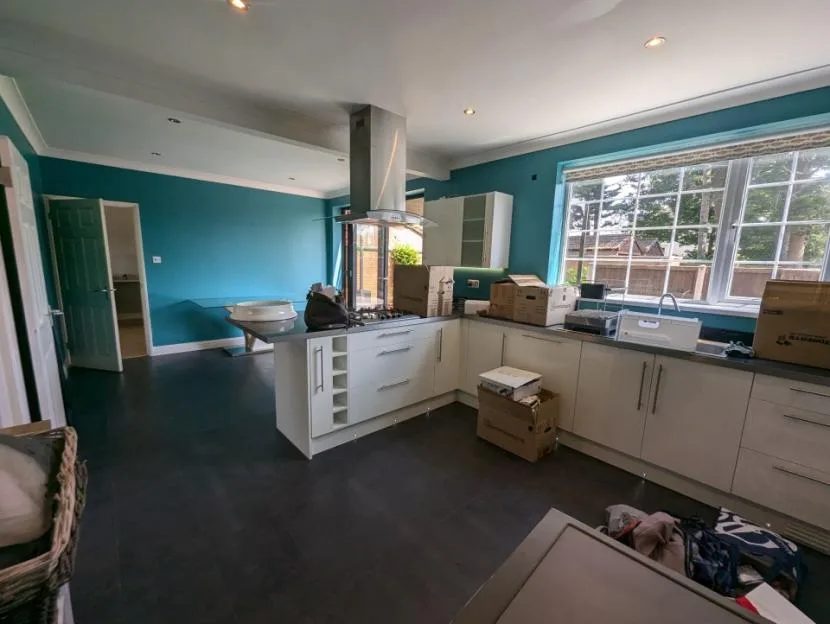 A kitchen with turquoise walls and white cabinets, filled with cardboard boxes during a move.
