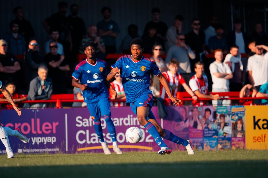 A Manchester United U21 player dribbles the ball downfield during a pre-season friendly against Altrincham.