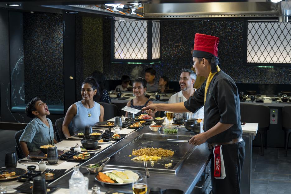 A chef cooking on a flat-top grill in front of a family at a restaurant on the Sun Princess cruise ship.