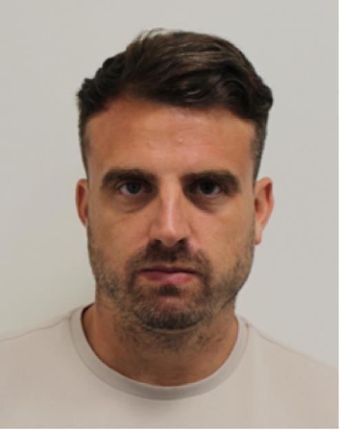 Mugshot of a man with short, dark hair and stubble, looking directly at the camera.
