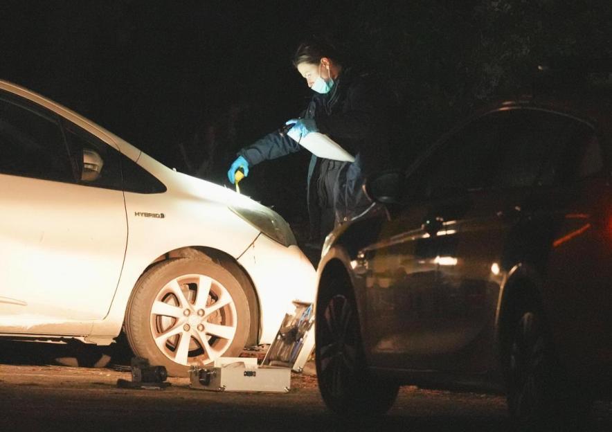 Forensic investigators examine a white car at night.