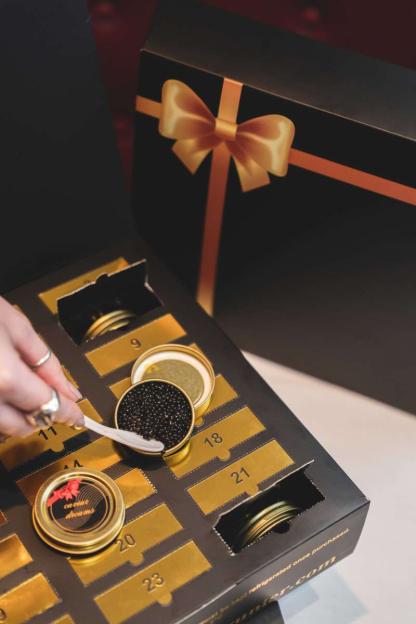 A person's hand opening a caviar advent calendar and scooping caviar from a small jar.