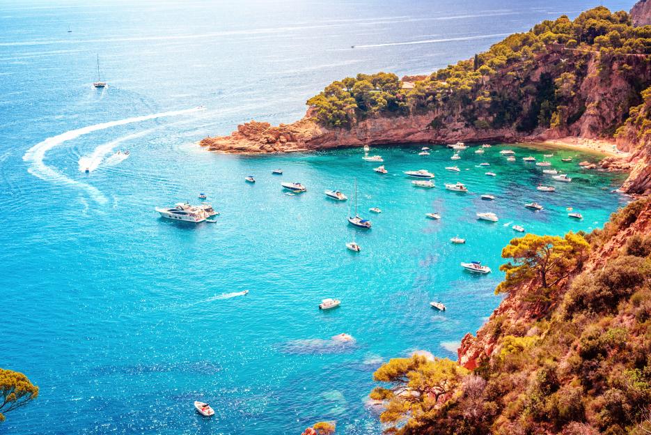 Elevated view of Cala Futadera near Tossa del Mar on the Costa Brava in Spain, with numerous boats in the turquoise water and on the beach.