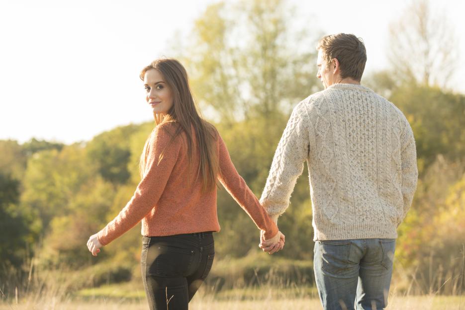 A young couple walking in a rural setting, holding hands.