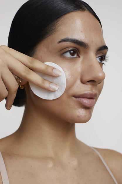 A young woman cleaning her face with a cotton pad.