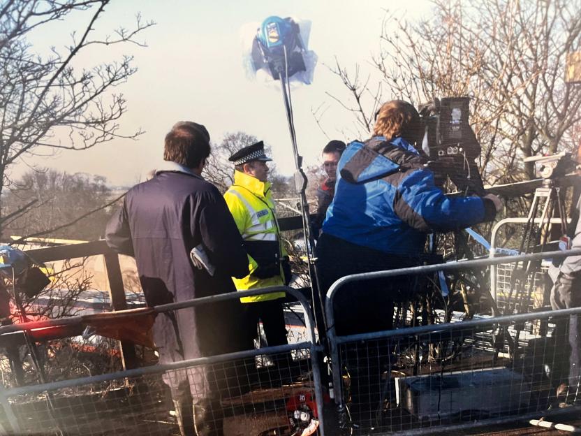 Police officer and camera crew at an outdoor filming location.