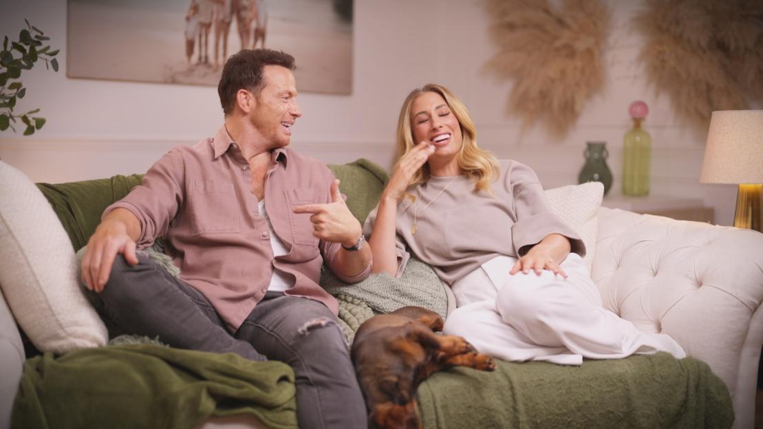 Stacey Solomon and Joe Swash laughing on a sofa with a dog.
