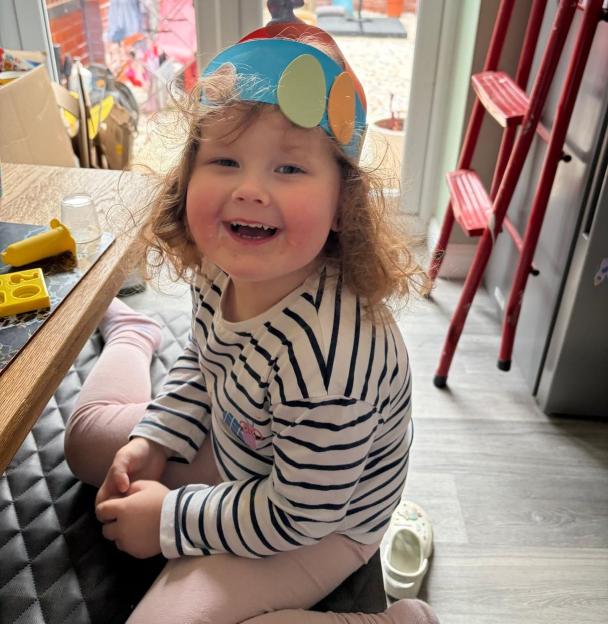 Penny Dunn, a young child, smiles at the camera while wearing a striped shirt and a festive headband.
