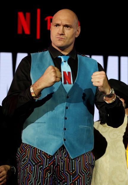 Tyson Fury at a press conference, wearing a blue vest and a tie with the Netflix logo.