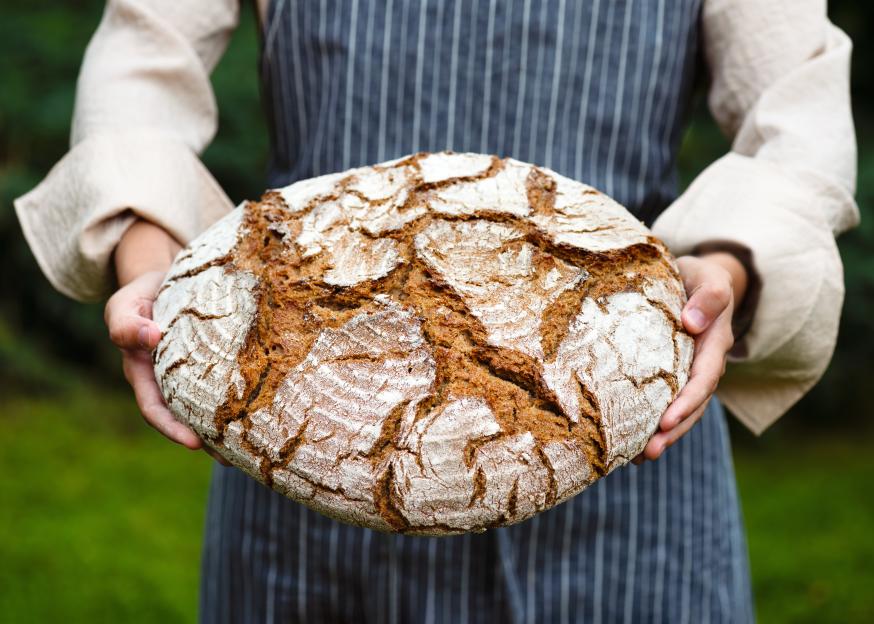Traditional handmade bread with a thick, cracked crust, resting in the hands of a baker. Its rustic appearance and artisanal charm celebrate slow food and natural ingredients.