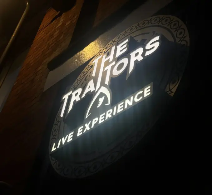 Neon sign for "The Traitors Live Experience" with a stylized bird head.