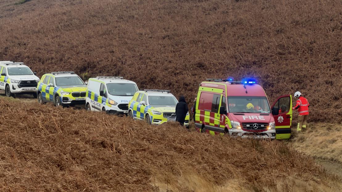 Emergency services vehicles, including police cars and a fire truck, parked on a moor.
