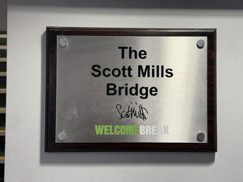 A plaque naming "The Scott Mills Bridge" with the DJ's signature and a Welcome Break logo.