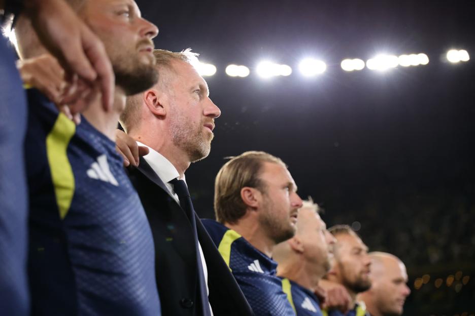 A row of Swedish soccer players and a coach standing on the field with stadium lights in the background.
