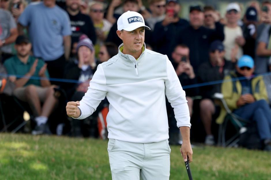 A golfer in a white cap and light-colored long-sleeved shirt celebrates with a fist pump.