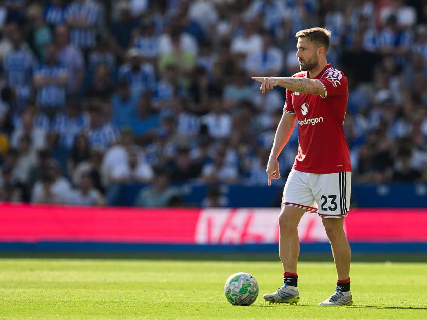 Luke Shaw in a Manchester United kit pointing on the field during a Premier League match.