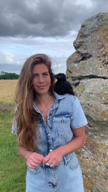 Hannah Bourne-Taylor standing with a crow on her shoulder next to a large rock.