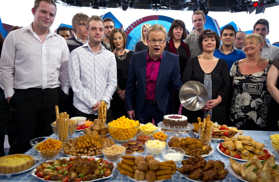 Steve Miller, a weight-loss expert, stands with a group of people behind a table overflowing with various party foods.
