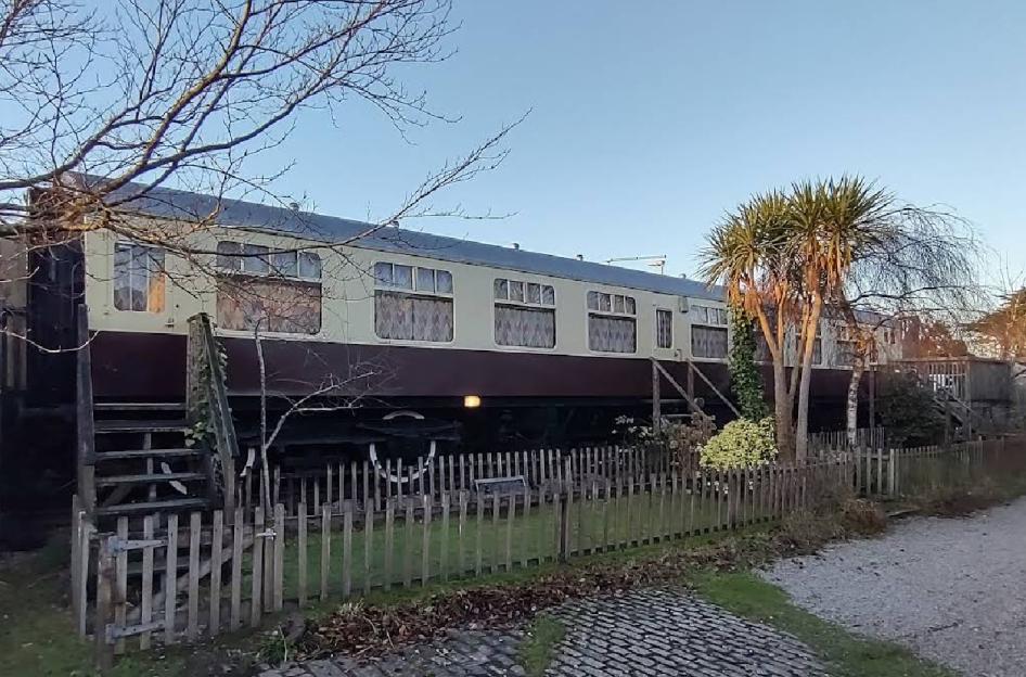 A train carriage converted into accommodation, with stairs leading up to its doors, behind a wooden fence.