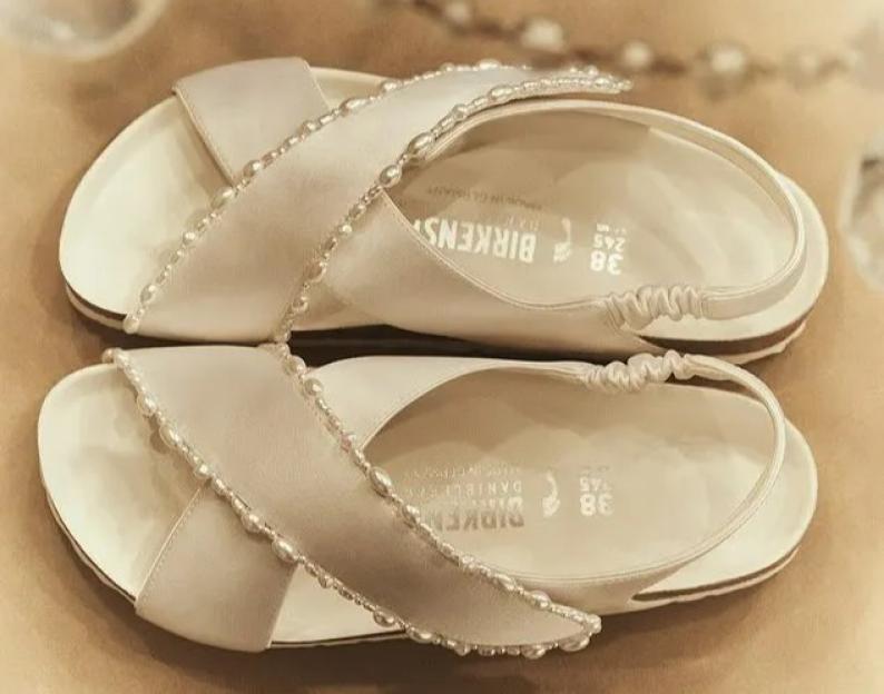 A pair of white Birkenstock sandals with pearl embellishments.