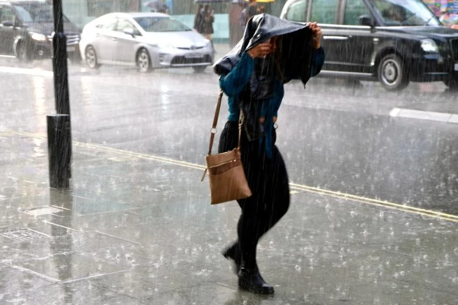 A woman walks down a city street during a heavy rain shower, using her jacket to cover her head.