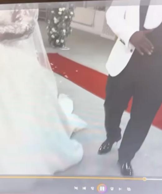 Screenshot of a wedding video showing the bride's white gown and the groom's black pants and white jacket, with a red carpet between them.