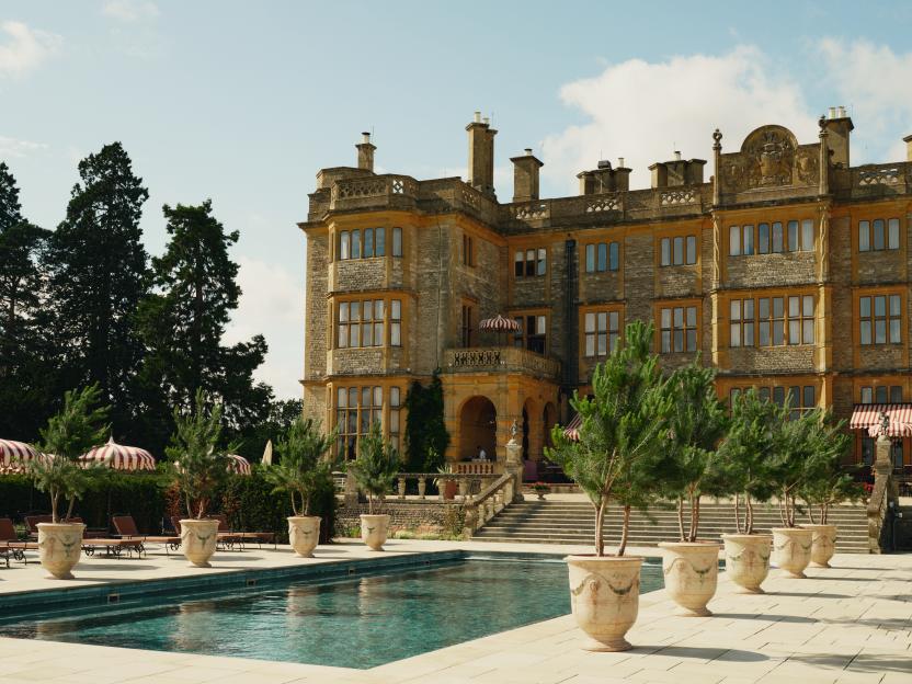 Estelle Manor in Oxfordshire, featuring a grand building with an outdoor swimming pool, lounge chairs, and potted trees.