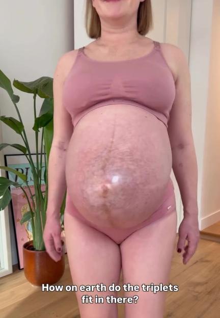 Pregnant woman showing her large baby bump while wearing a pink bra and underwear.