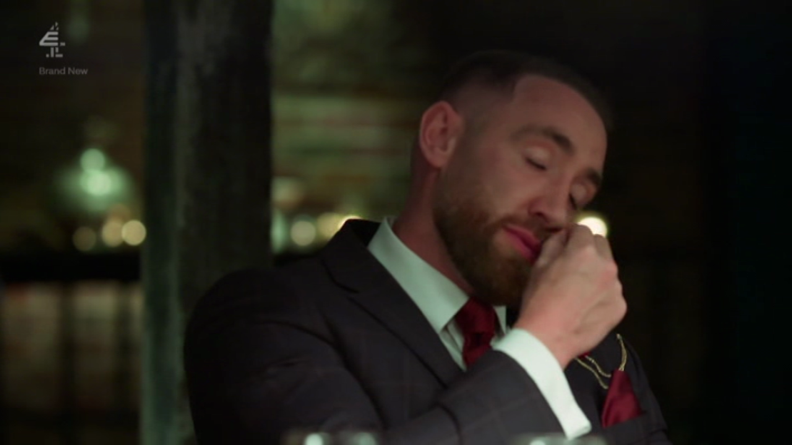 Man in a suit with his eyes closed and hand near his mouth, appearing emotional.