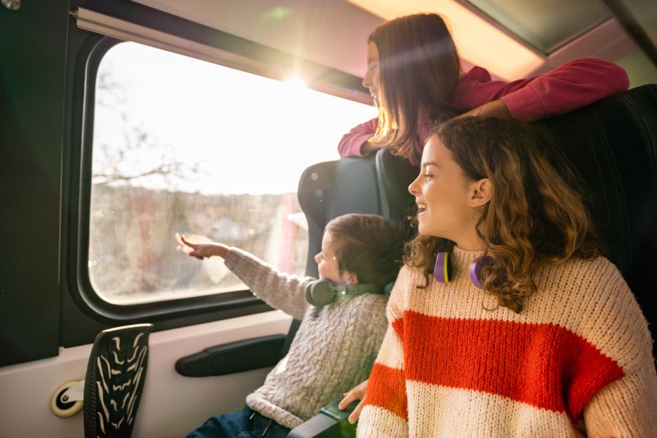 Three happy kids traveling by train and looking out of the window, with sunlight shining through.