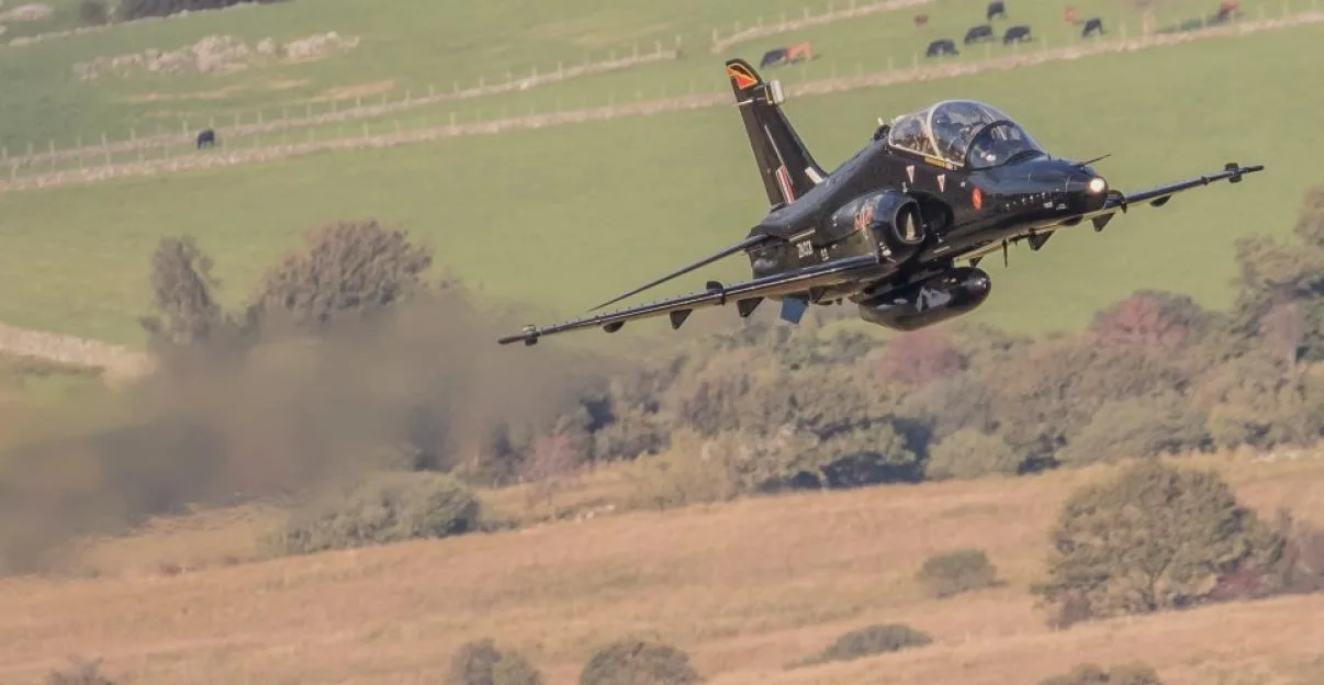 A British Aerospace Hawk military training aircraft of the UK's Royal Air Force flying at low altitude over open countryside.