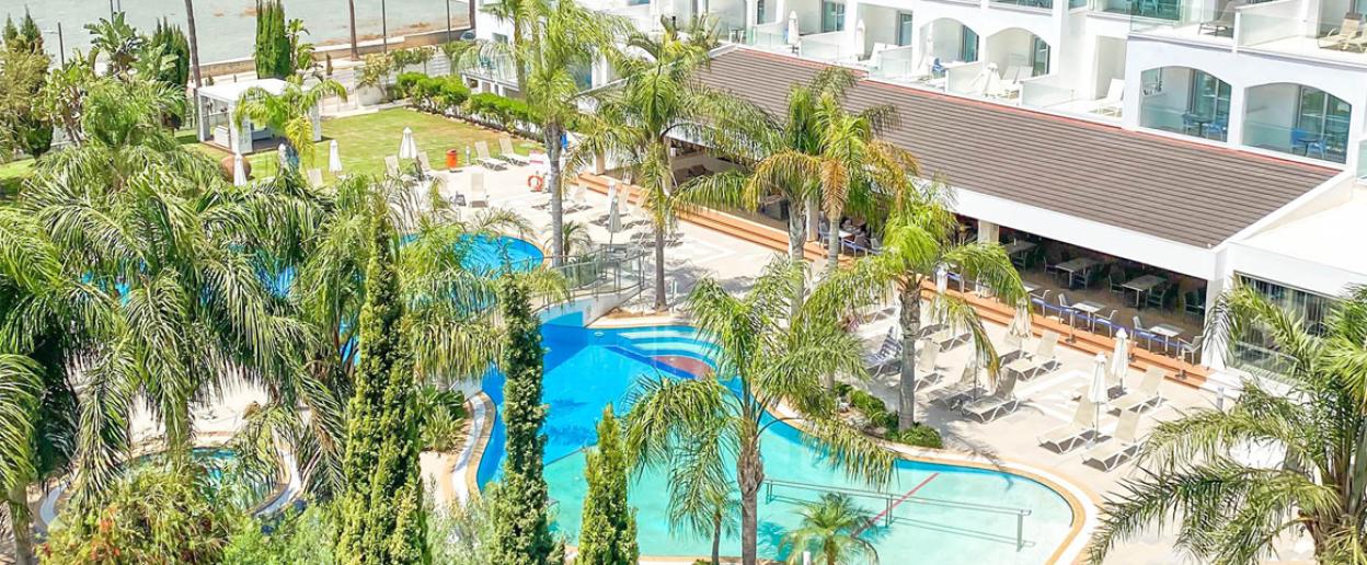 Aerial view of Anesis Hotel in Ayia Napa, Cyprus, showing swimming pools, palm trees, and outdoor seating.