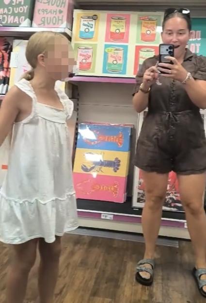 Amy Harrowven recording her daughter in a store, holding a phone to capture her reflection in a mirror.