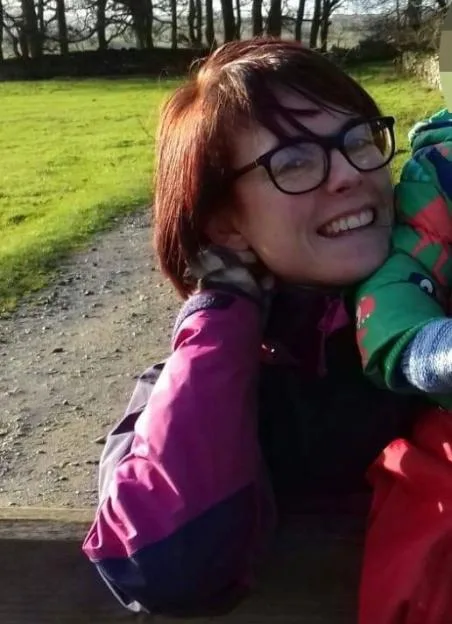 Aimee Jones outdoors, wearing glasses and a purple jacket.