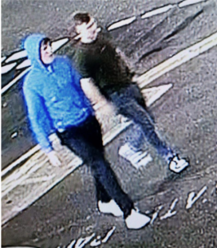 Two males captured from a surveillance camera, one in a blue hoodie and the other in a dark shirt and jeans.