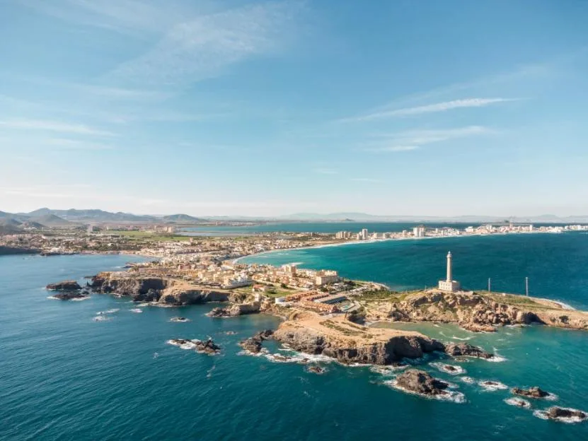 Aerial drone view of Cabo de Palos and La Manga in Spain, featuring a coastal town and lighthouse surrounded by the Mediterranean Sea.