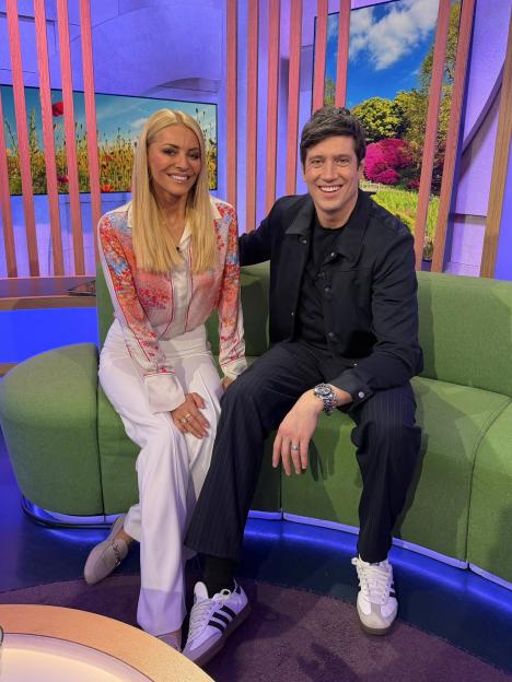 Tess Daly and Vernon Kay sitting together on a green couch on The One Show set.