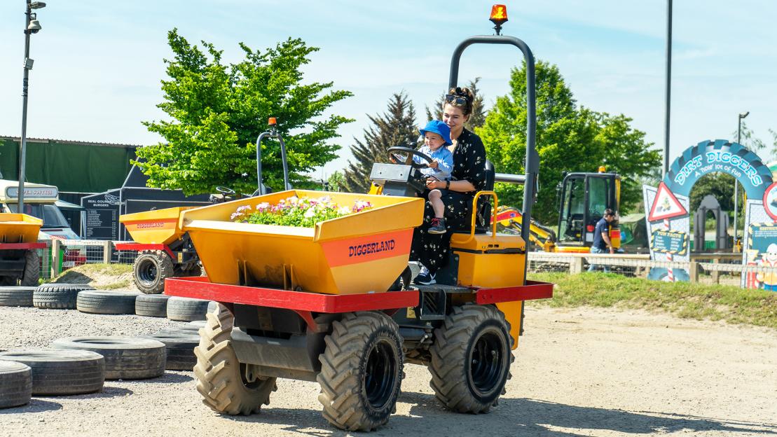 A woman and a child in a blue hat ride a yellow Diggerland amusement park vehicle.