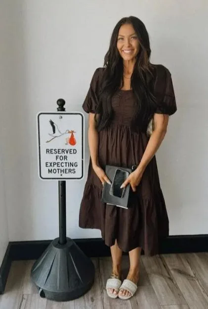 Stacey Solomon smiles while standing next to a reserved parking space sign for expecting mothers.