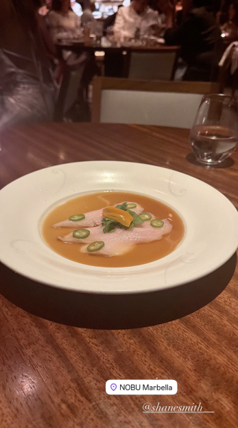 A plate of raw fish with chili slices and sauce on a wooden table.