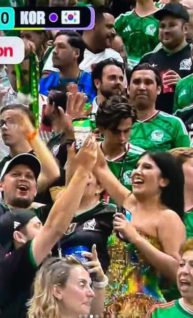 A woman in a vibrant, strapless dress cheers in a stadium crowd, with others around her also showing excitement.